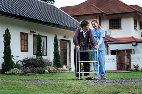 Nurse Or Caregiver Helps Elderly Walk By Using Walker In Garden Stock