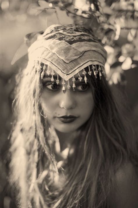 a woman with long hair wearing a headdress and beads on her face is standing in front of a tree