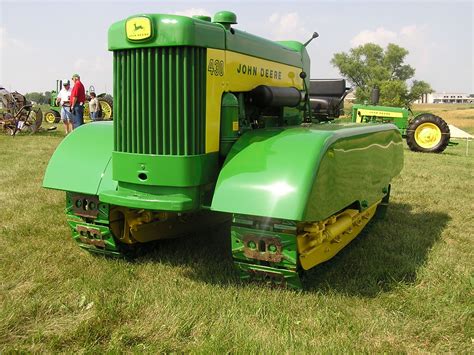 A Large Green Tractor Parked On Top Of A Lush Green Field Next To Other