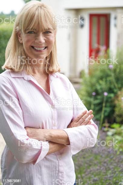 Portrait Of Mature Woman Standing In Garden In Front Of Dream Home In