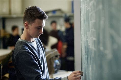 Young Man Student Writing On The Blackboard Of The Classroom Del