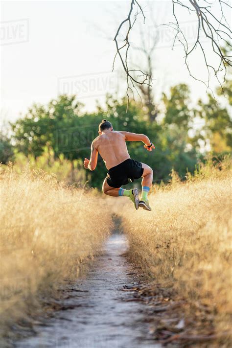 Full Body Back View Of Unrecognizable Shirtless Male Athlete Jumping High Over Narrow Footpath