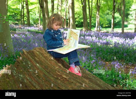 Young Girl Reading Book In Bluebell Wood Norfolk England Stock Photo