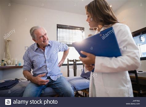 Senior Male Patient Showing Back Ache To Female Therapist With File At