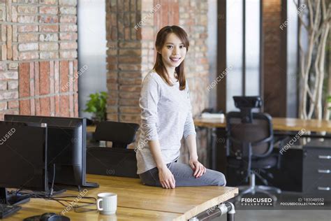 Chinese Woman Sitting On Desk In Office — Casual Business People
