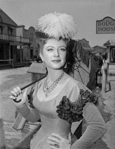 An Old Photo Of A Woman In A Dress And Feathered Hat Posing For The Camera