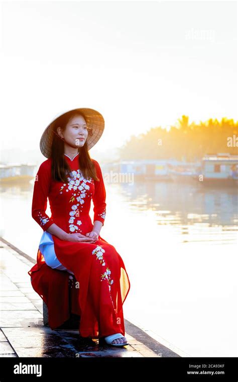 eine junge asiatische frau in einem roten ao dai kleid und konischen hut lächelnd und sitzt