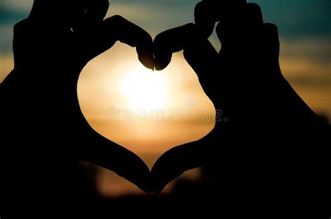 silhouette of a girl s hands with heart shaped love heart shape made with hands at sunset stock