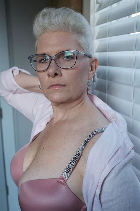An Older Woman Wearing Glasses And A Pink Top Is Leaning Against A