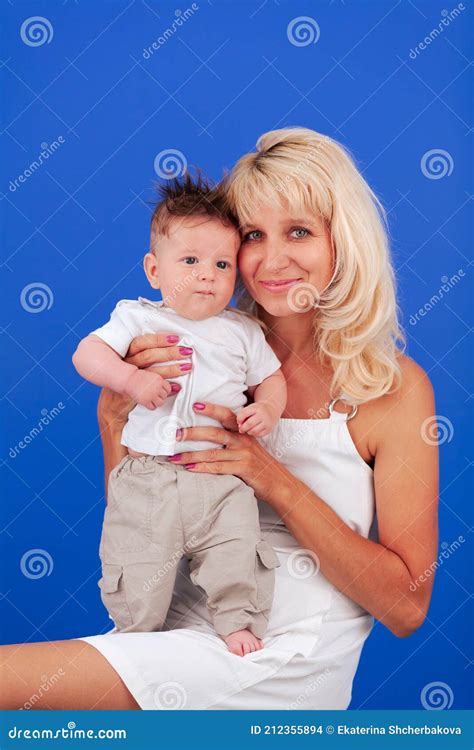 Mom Blonde With Young Son In Her Arms Sits On A Blue Background Stock
