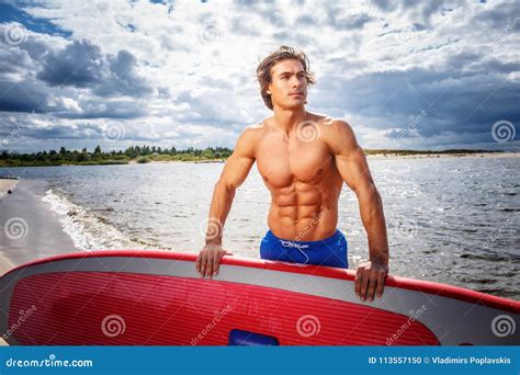 Surfer Male With A Muscular Body With His Surfboard At The Beach