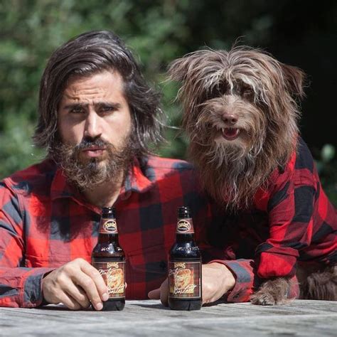 A Man With Long Hair And Beard Holding Two Beer Bottles Next To A Small Dog
