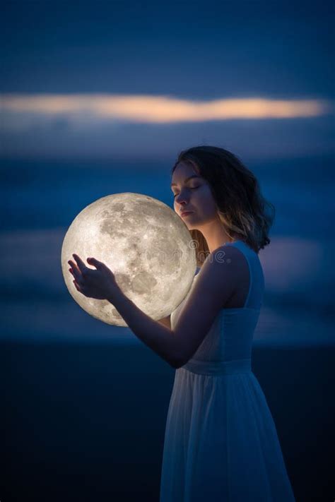 Λεπτή εικόνα ενός αγγέλου ενός κοριτσιού με το φεγγάρι στα χέρια της στη νυχτερινή παραλία