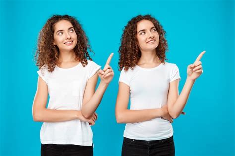 Free Photo Two Girls Twins Smiling Pointing Fingers Away Over Blue Wall