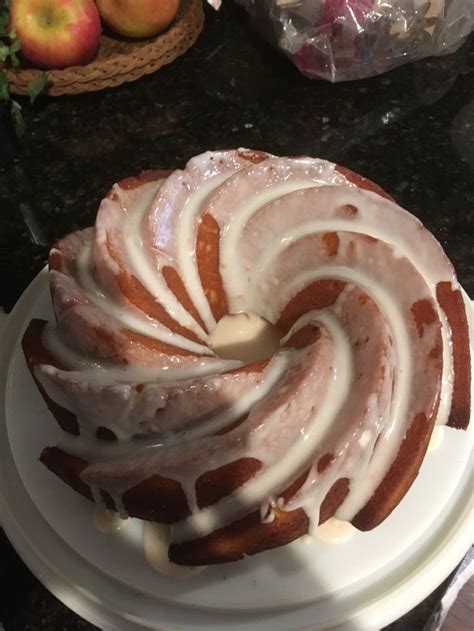 A Bundt Cake With Icing Sitting On Top Of A Table Next To Apples
