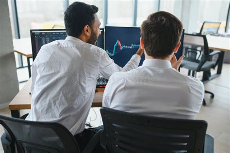 Two Men Traders Sitting At Desk At Office Together Monitoring Stocks