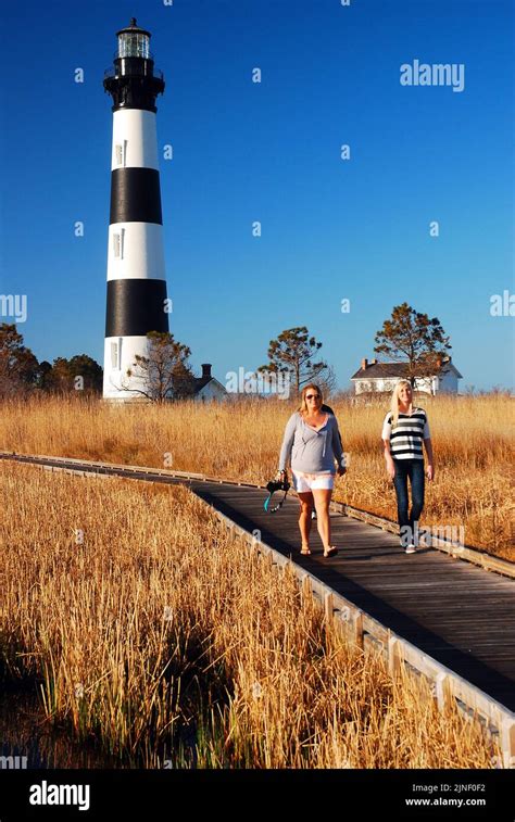 Two Women Walk On The Boardwalk As It Travels Through A Swamp Area Near