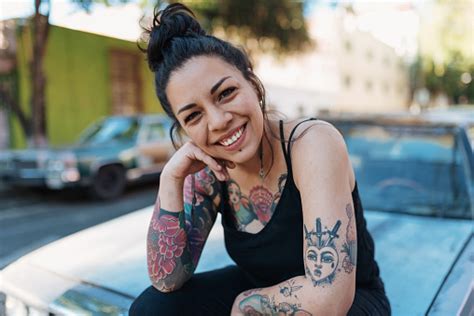 Portrait Of Beautiful Latina Mexican Millennial Woman With Tattoos Sitting On Car Hood Stock