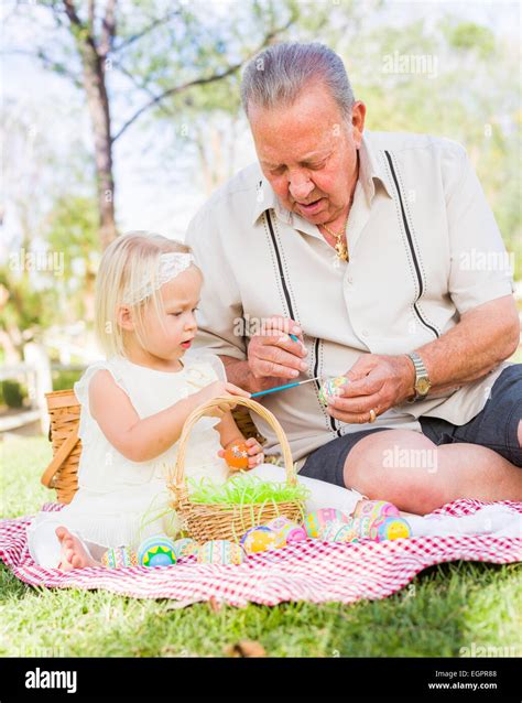 Loving Grandfather And Granddaughter Coloring Easter Eggs Together On Picnic Blanket At The Park