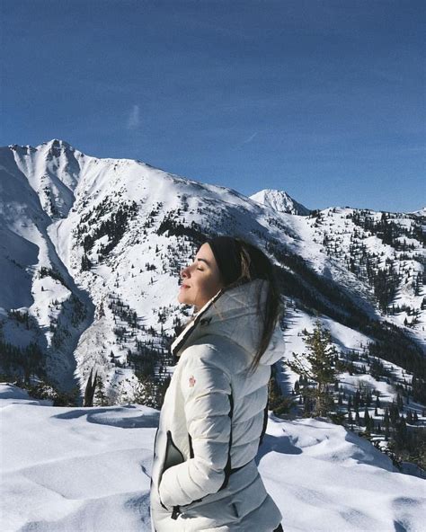 A Woman Standing On Top Of A Snow Covered Slope With Mountains In The