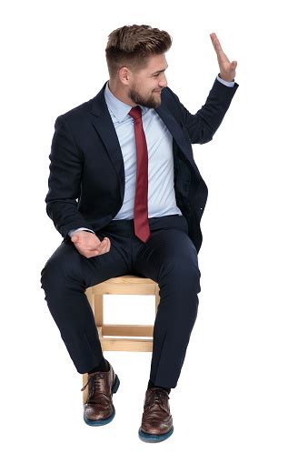 Happy Young Businessman Saluting And Sitting In Studio Stock Photo