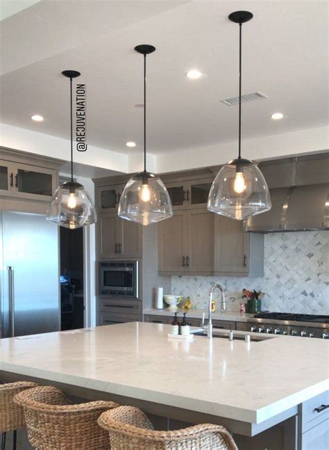 A Kitchen Island With Three Hanging Lights Above It And Wicker Chairs