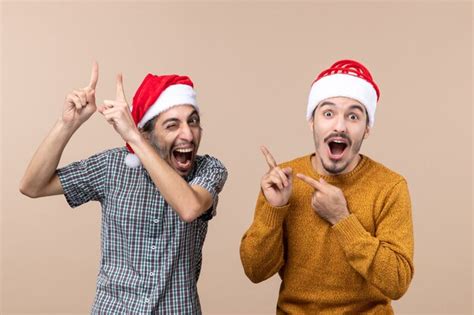 베이지 색 격리 된 배경에 다른 뭔가를 보여주는 산타 모자 하나 전면보기 두 기뻐하는 사람 무료 사진
