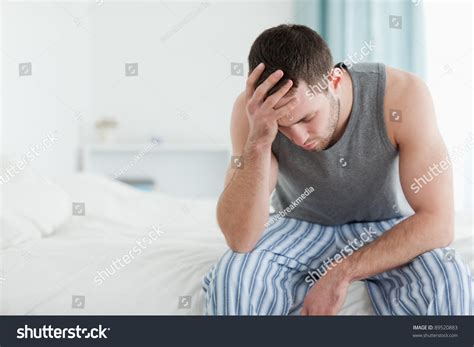 Sad Man Sitting On His Bed With His Head On His Hand Stock Photo