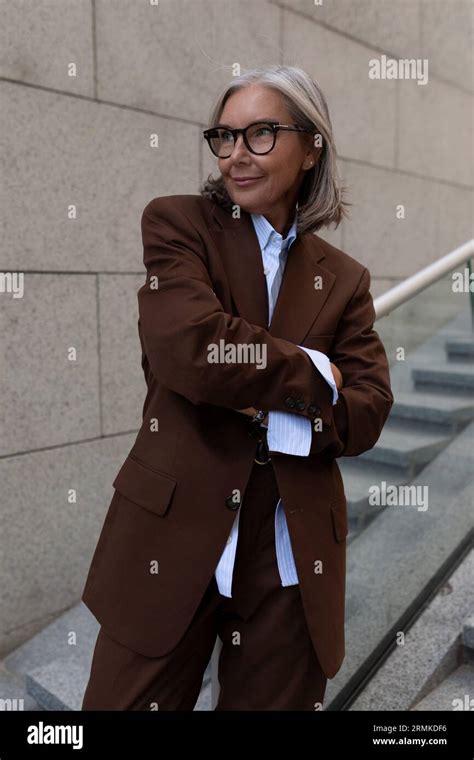 well groomed slender mature business woman with gray hair is dressed in a brown suit in a city