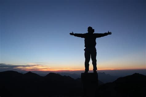 Anonymous Male Climber Standing On Mountain Top With Outstretched Arms