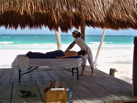 a woman getting a back massage on the beach under a thatched roof over looking the ocean