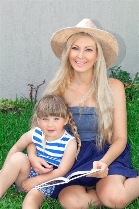 Mom Blonde And Babe Are Lying On The Grass And Reading A Book Happy Family Stock Photo