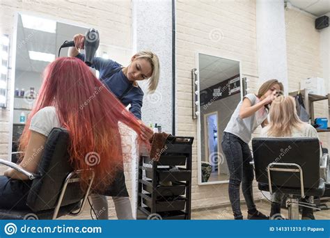 female hairdressers serve women clients in the hairdresser`s salon one dries her hair and the