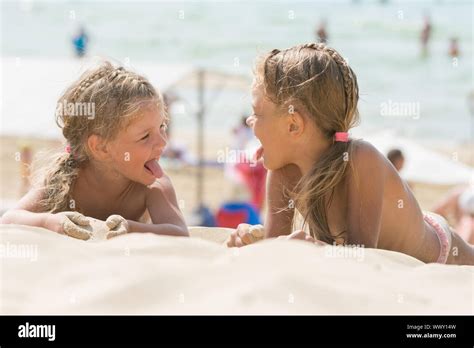 Two Happy Little Girls Show Each Other Tongues On A Sandy Beach Stock
