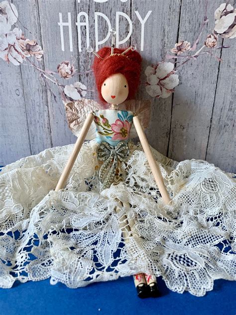 a doll with red hair sitting on top of a white lace doily next to a wooden sign