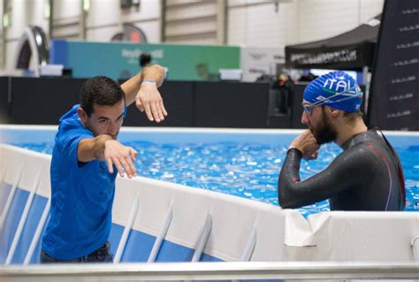 Two Men In Wetsuits Standing Next To A Swimming Pool And Pointing At Something