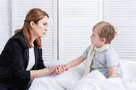 Side View Of Mother Taking Care Of Sick Son In Bedroom They Holding Hands And Looking At Each