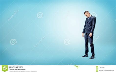 A Sad Businessman Standing On Blue Background Looking Down With Slumped
