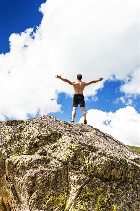 Young Man Standing On Top Of A Cliff With Arms Raised Stock Photo