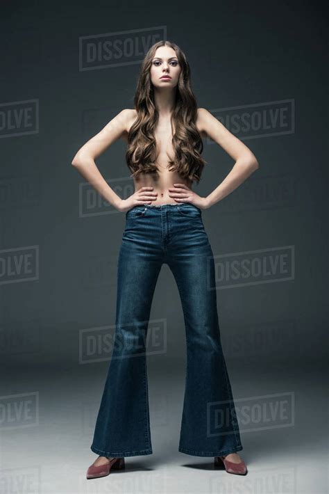 Beautiful Half Naked Girl With Long Hair Posing In Flare Jeans On Grey