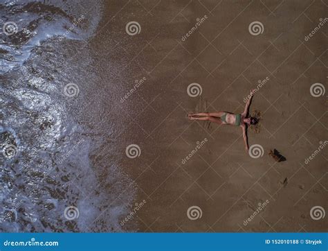 Aerial Top View Of Woman With Her Hands Outstretched Laying On The Sandy Beach Stock Photo