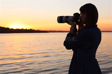 Young Female Photographer Taking Photo Of Riverside Sunset With
