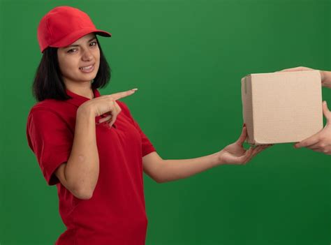 Repartidor Joven En Uniforme Rojo Y Gorra Dando Caja De Cartón A Un Cliente Confundido Y