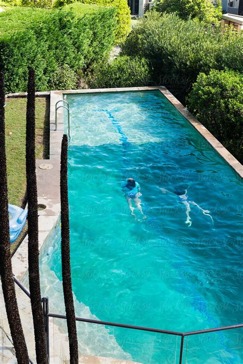 Two Teen Girls Swimming In A Large Backyard Pool By Gillian Vann