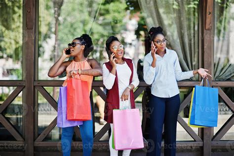 Three Casual African American Girls With Colored Shopping Bags Walking