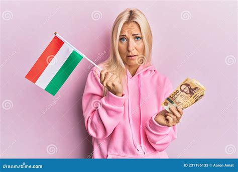 Young Blonde Woman Holding Hungary Flag And Forint Banknotes Clueless And Confused Expression