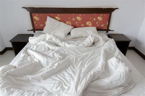 Untidy Unmade Bed With Two Messy Pillows And A White Crumpled Blanket In A Hotel Stock Photo