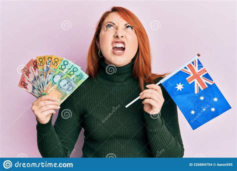 Beautiful Redhead Woman Holding Australian Dollars And Australia Flag Angry And Mad Screaming