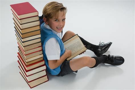 Schoolboy Reading Book While Sitting Against Books Stack On White