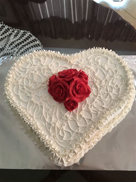 a white heart shaped cake with red roses on top